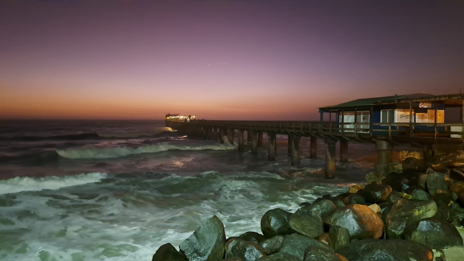 The pier at Swakopmund at dusk — the restaurant lit at the far end, the Atlantic rough below
